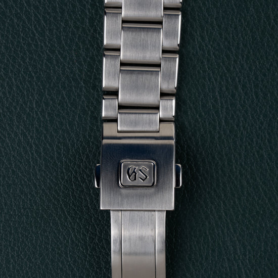 Grand Seiko Heritage Collection SBGV221 - Close-up van de vouwsluiting met GS-logo op de stalen schakelband